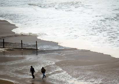 People walk near a surf from Hurricane Sandy rising past sand fences onto the beach in Ocean City, Maryland 