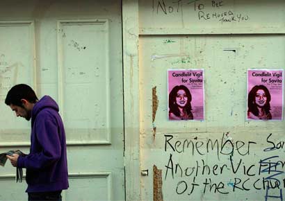A man reads a newspaper next to posters advertising a candlelit vigil at the University Hospital Galway in Galway, Ireland