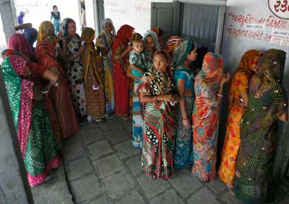 Women stand in a queue to cast their ballots outside a polling booth during the first phase of state elections in Sanand