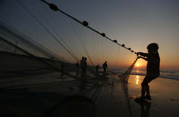 A Palestinian boy pulls a fishing net as the sun sets on a beach in Gaza City
Photo by Suhaib Salem