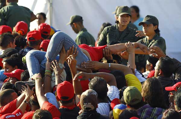 A supporter of Venezuela's late President Hugo Chavez is lifted out of the crowd after fainting while waiting for a chance to view his body in state, at the military academy in Caracas March 8, 2013. Chavez will be embalmed and put on display 