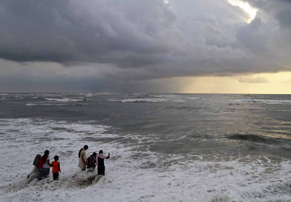 Beachgoers walk in the waters at Fort Kochi beach as clouds hover over the Arabian Sea in the southern Indian state of Kerala. Photo by Sivaram V