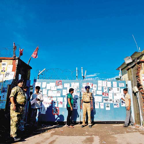 Security personnel stand guard at an entrance gate, covered with posters of missing pilgrims, of the Jolly Grant Airport in Dehradun.