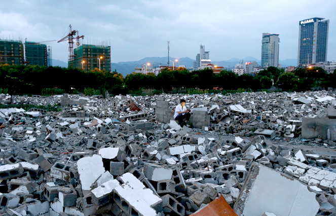 A cook from a nearby hotel looks at his mobile phone at a demolition site, which is making way for the building of new property in Lishui, Zhejiang province, China, on June 10, 2014. Reuters/Stringer china-demolition